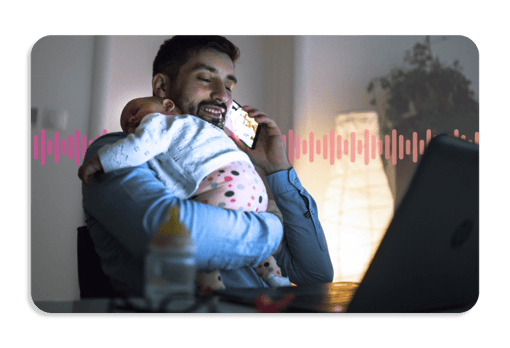 A smiling father holding a sleeping child while using a mobile phone